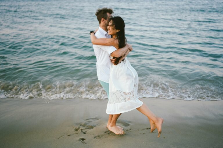 A couple embraces on a sandy beach by the ocean.